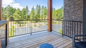 A wooden deck with a stone wall, a black metal railing, and a view of a parking lot and trees. - Central Condo with Suncadia Pool Access (Cle Elum)