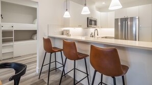 A modern kitchen with a white countertop, stainless steel appliances, and three brown bar stools. - Golf View Condo & Suncadia Pool Access (Cle Elum)