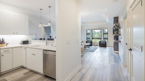A modern kitchen with white cabinets, a dishwasher, and a dining area with a gray sofa and a table. - Golf View Condo & Suncadia Pool Access (Cle Elum)
