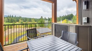 A balcony with a table and chairs, overlooking a green landscape with trees and a cloudy sky. - Golf View Condo & Suncadia Pool Access (Cle Elum)
