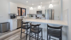 A modern kitchen with white cabinetry, stainless steel appliances, and a central island with bar stools. - Golf View Condo & Suncadia Pool Access (Cle Elum)