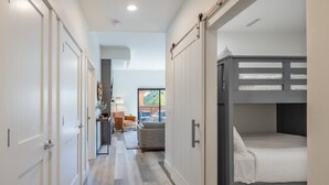 A narrow hallway with a bunk bed on the right, a desk with a chair, and a sofa in the background. - Golf View Condo & Suncadia Pool Access (Cle Elum)