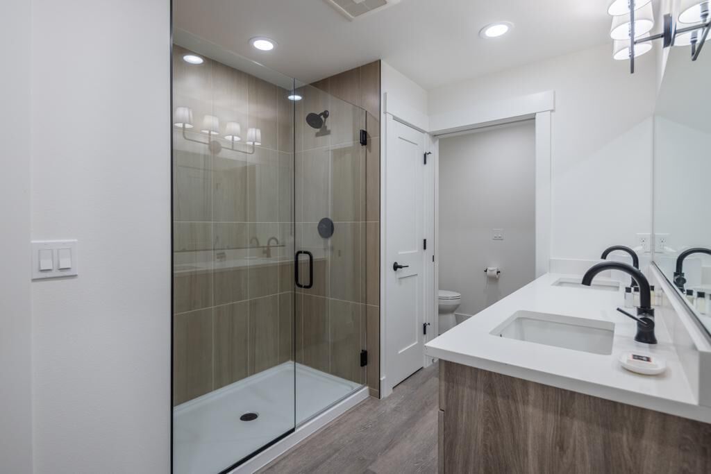 A modern bathroom with a glass-enclosed shower, a white sink with a black faucet, and a large mirror.