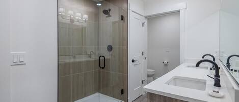 A modern bathroom with a glass-enclosed shower, a white sink with a black faucet, and a large mirror.