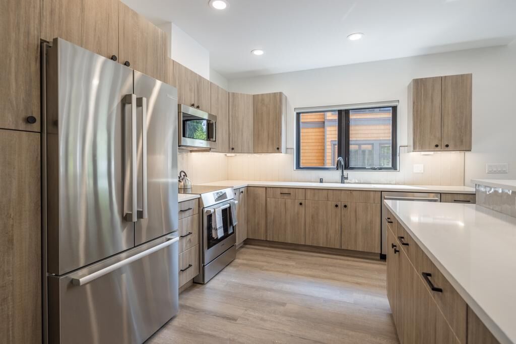 A modern kitchen with wooden cabinets, stainless steel appliances, and a large window providing natural light.