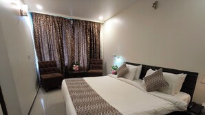 A modern bedroom with a large bed, two brown armchairs, a small table with a vase of flowers, and patterned curtains. - Hotel Heritage 2001-Nagpur (Nagpur)