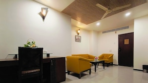 A hotel room with a desk, two yellow armchairs, a small table, and a ceiling fan. - Hotel Heritage 2001-Nagpur (Nagpur)