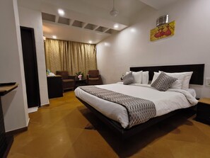 A hotel room with a large bed, a desk with a chair, a small table with a vase, and a painting on the wall. - Hotel Heritage 2001-Nagpur (Nagpur)