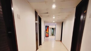 A long, narrow hallway with white walls and a tiled floor. There are doors on both sides, some with dark frames. The hallway is well-lit with ceiling lights. - Hotel Heritage 2001-Nagpur (Nagpur)