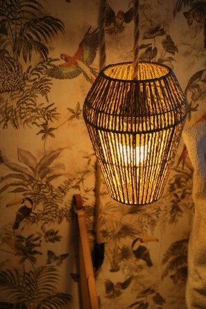 A hanging light fixture with a woven design, set against a wall with a bird and plant mural. - Maison Bossanne (Barbières)