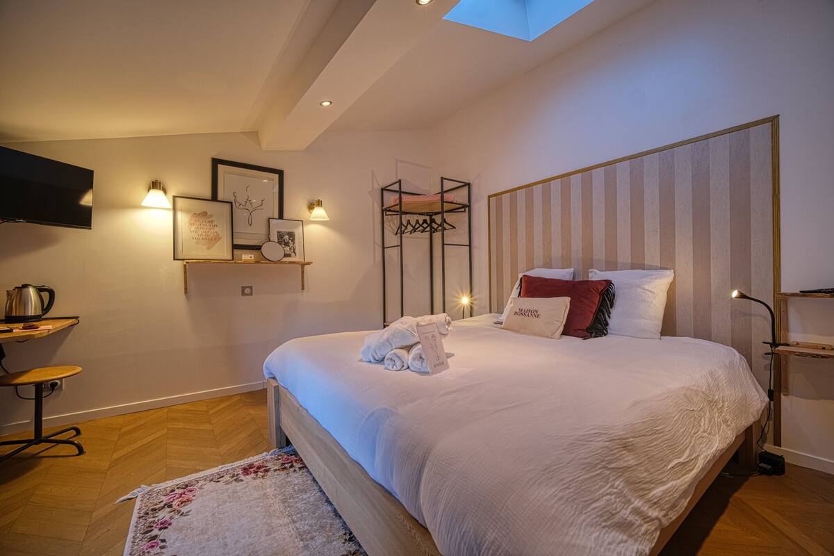 A neatly arranged bedroom with a bed, bedside tables, a TV, and a skylight.