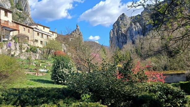 A stone building with balconies, surrounded by lush greenery and a rocky mountain backdrop.