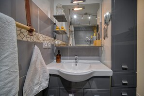 A modern bathroom with a white sink, grey cabinets, and a mirror above the sink. - Maison Bossanne (Barbières)