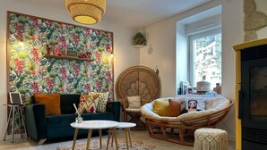 A cozy living room with a teal sofa, a wicker chair, a round coffee table, and a large floral wallpaper.