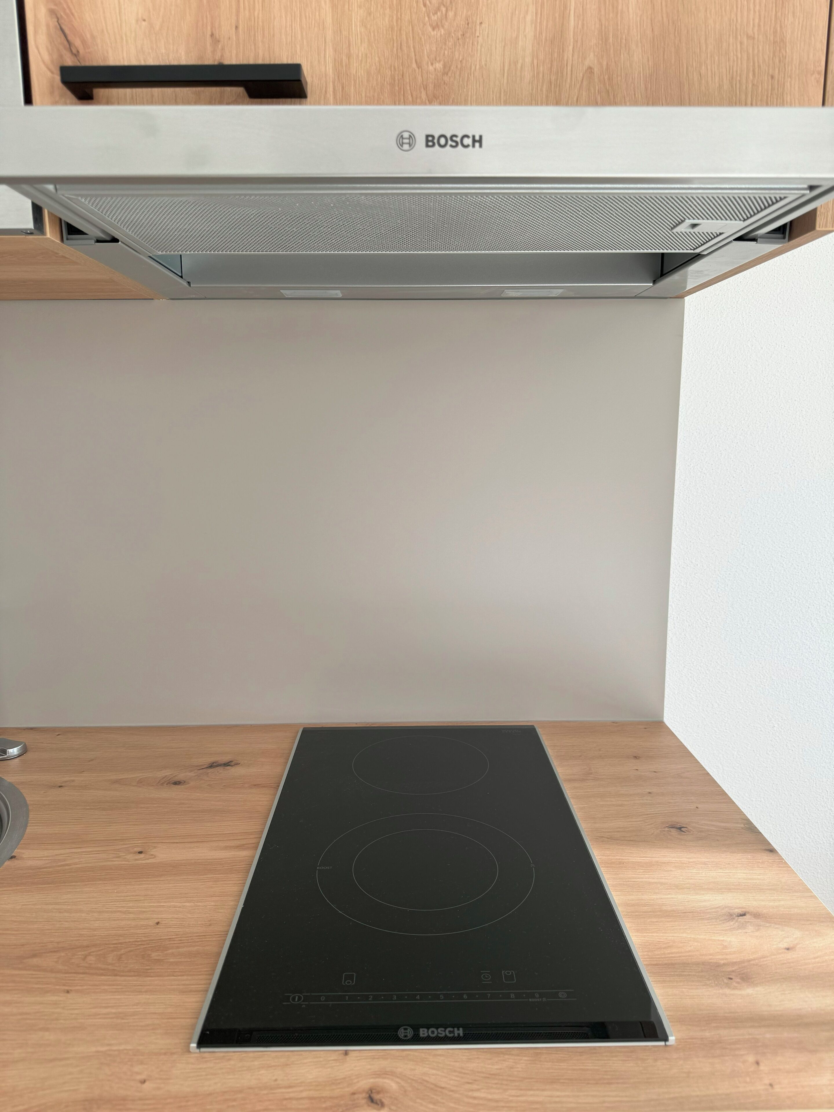 A Bosch induction cooktop in a kitchen with wooden cabinets and a white wall.