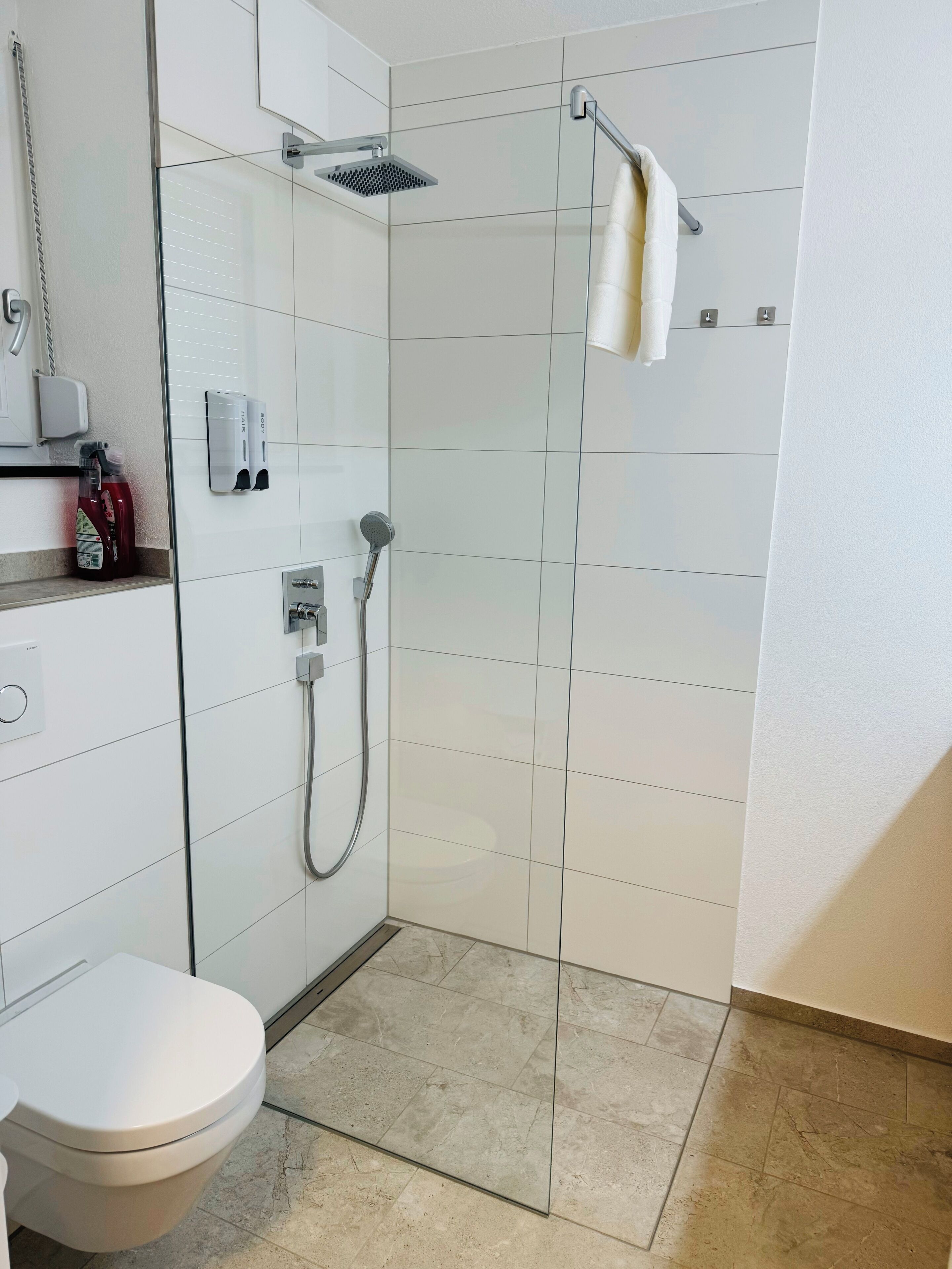 Un baño moderno con ducha de vidrio, inodoro y lavamanos con dispensadores de jabón.