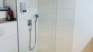Un baño moderno con ducha de vidrio, inodoro y lavamanos con dispensadores de jabón.