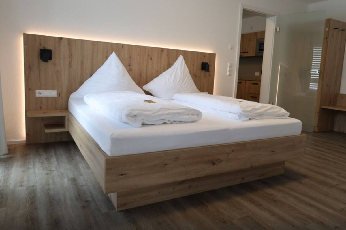 A modern bedroom with a wooden headboard, a large bed with white linens, a wooden floor, and built-in storage cabinets.