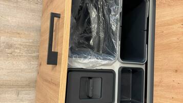 Eine Holzkassette mit mehreren Fächern, darunter eine transparente Plastiktüte und eine schwarze Ablagefläche.