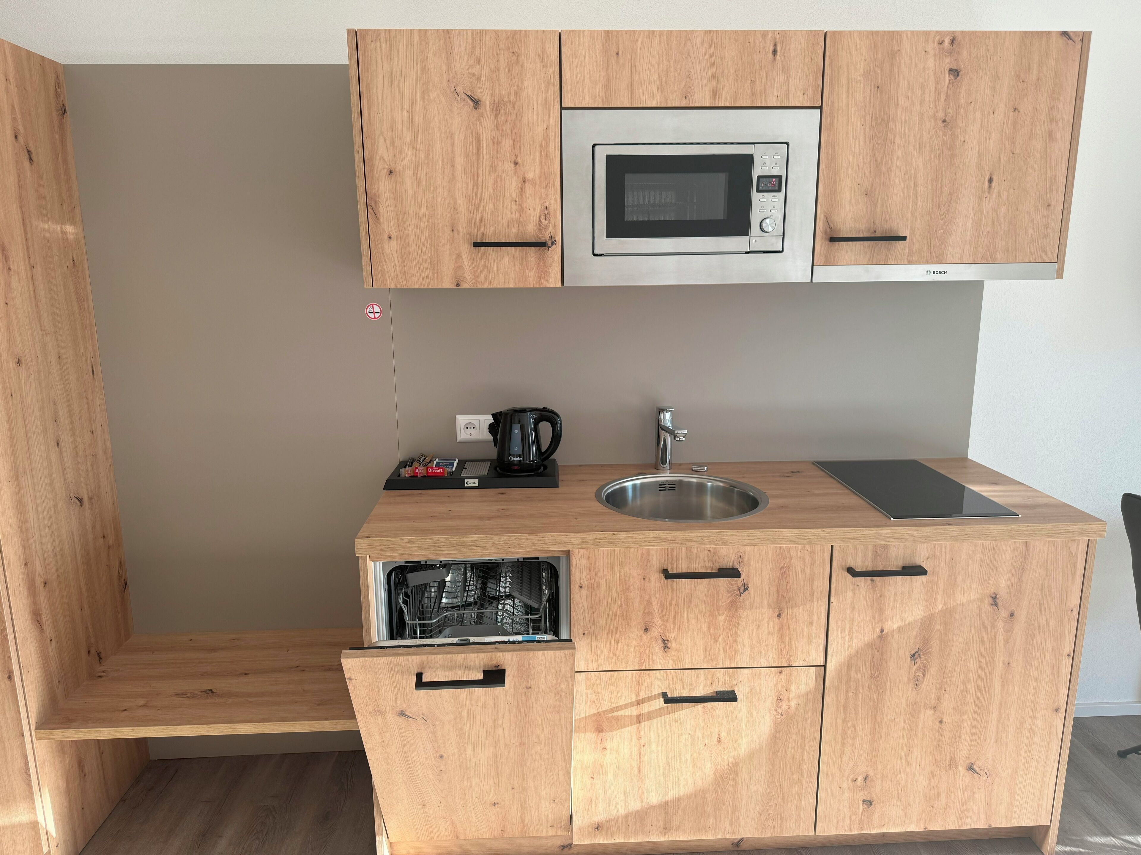 A compact kitchenette with a built-in microwave, a kettle, a sink, and a dishwasher.