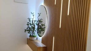 A modern interior with a wooden slatted wall, a round mirror, and a small plant on a wooden shelf.