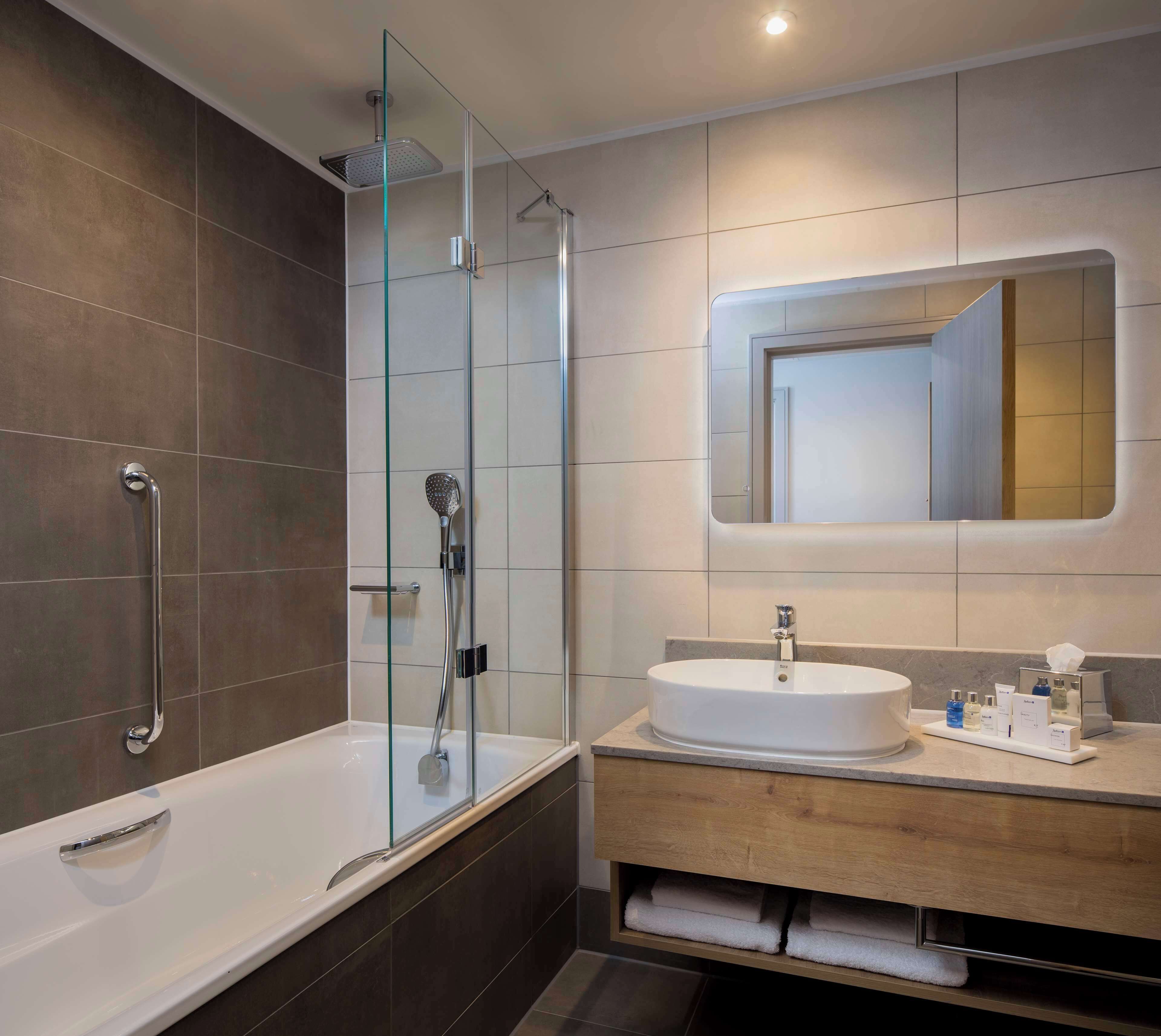 Une salle de bain moderne avec une douche à parois de verre, une baignoire blanche et un meuble-lavabo doté d’un grand miroir.