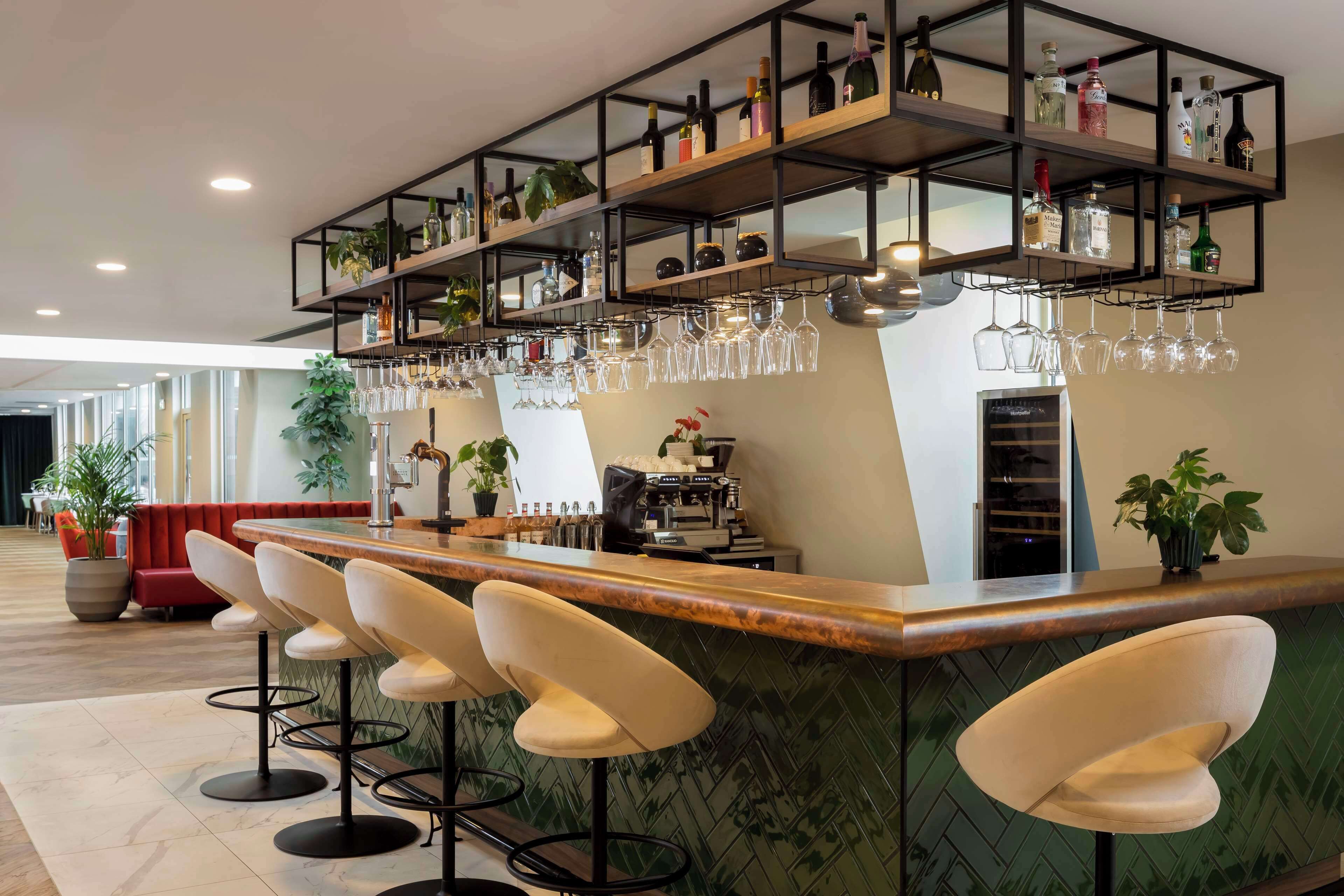 A bar area with multiple stools, shelves with bottles and glasses, and a coffee machine.