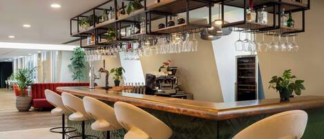 Een bar met meerdere krukken, planken vol flessen en glazen, en een koffieapparaat.