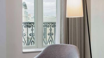 Une chambre moderne avec un fauteuil gris, une lampe sur pied et une fenêtre donnant sur un immeuble et un balcon.