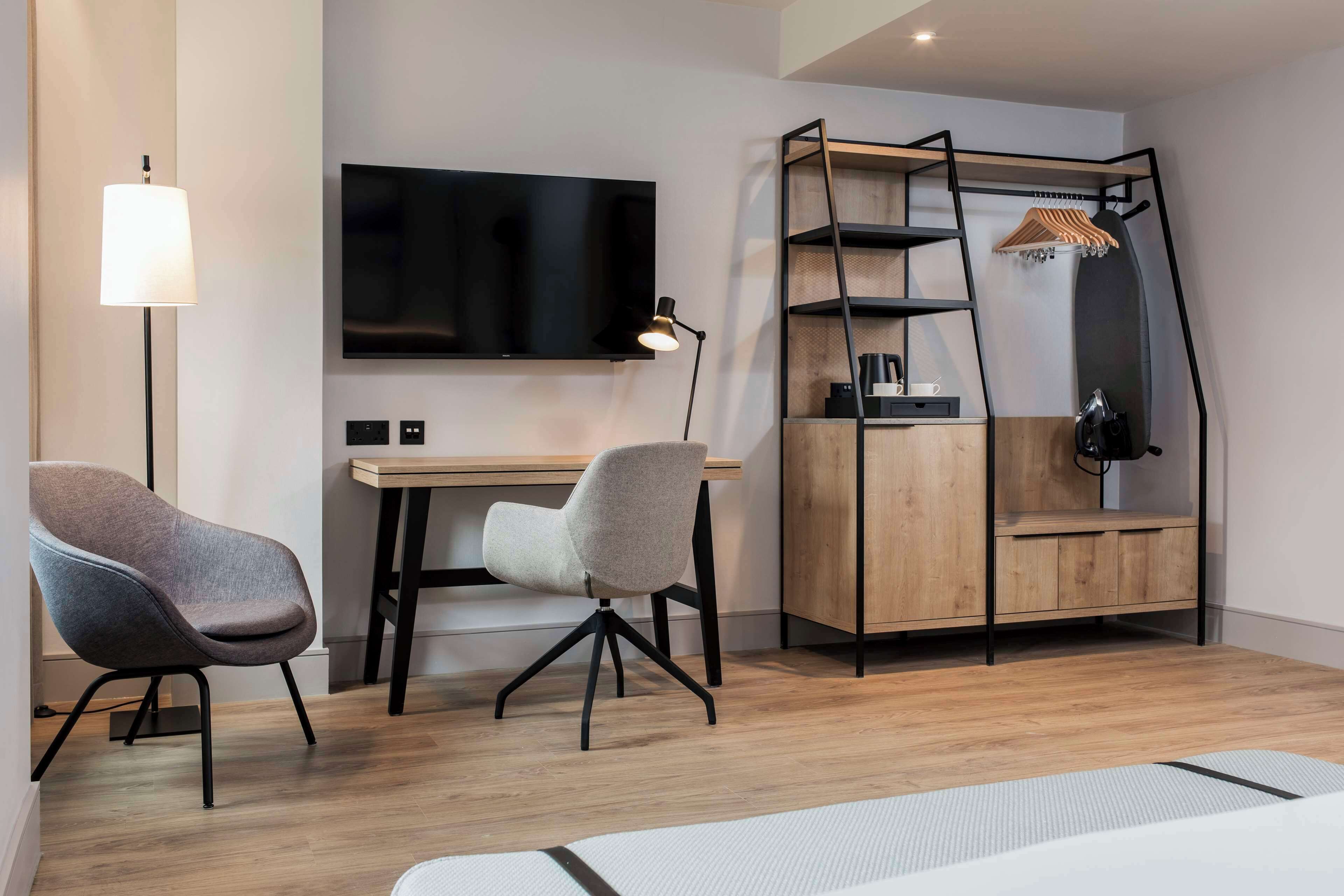 A modern room with a desk, two chairs, a TV, a lamp, and a wooden cabinet with shelves.