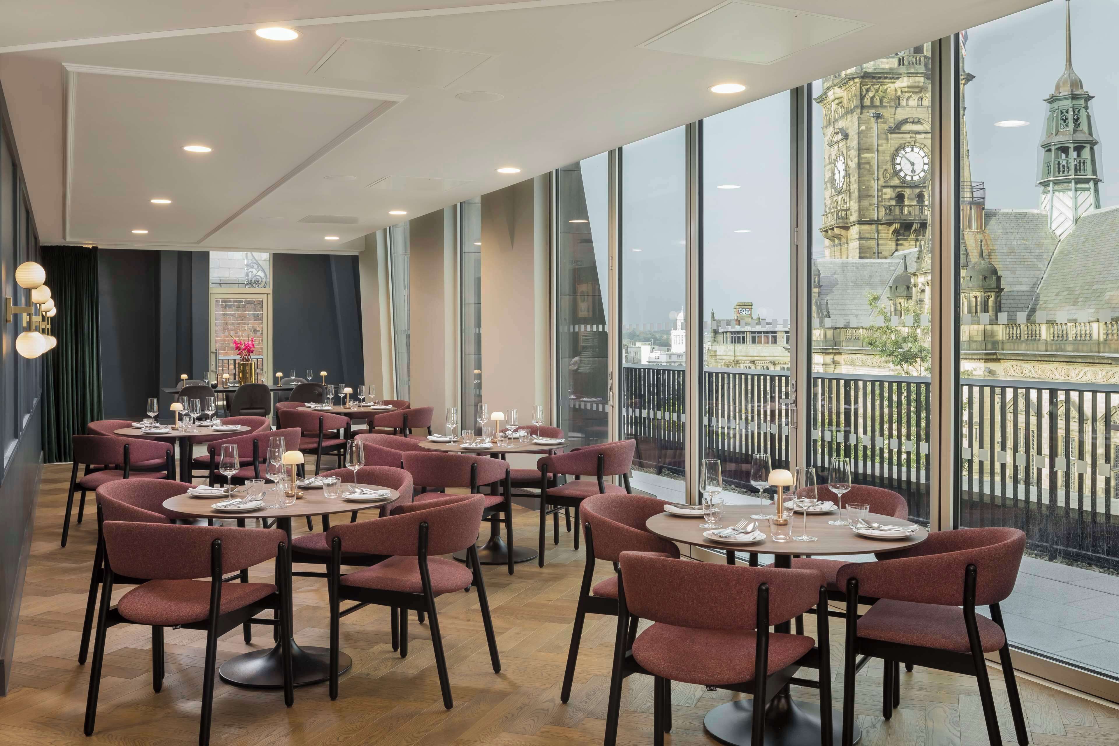 A restaurant with round tables and chairs, large windows with a view of a historic building.
