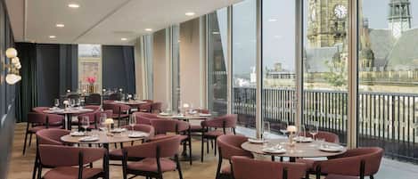 A restaurant with round tables and chairs, large windows with a view of a historic building.