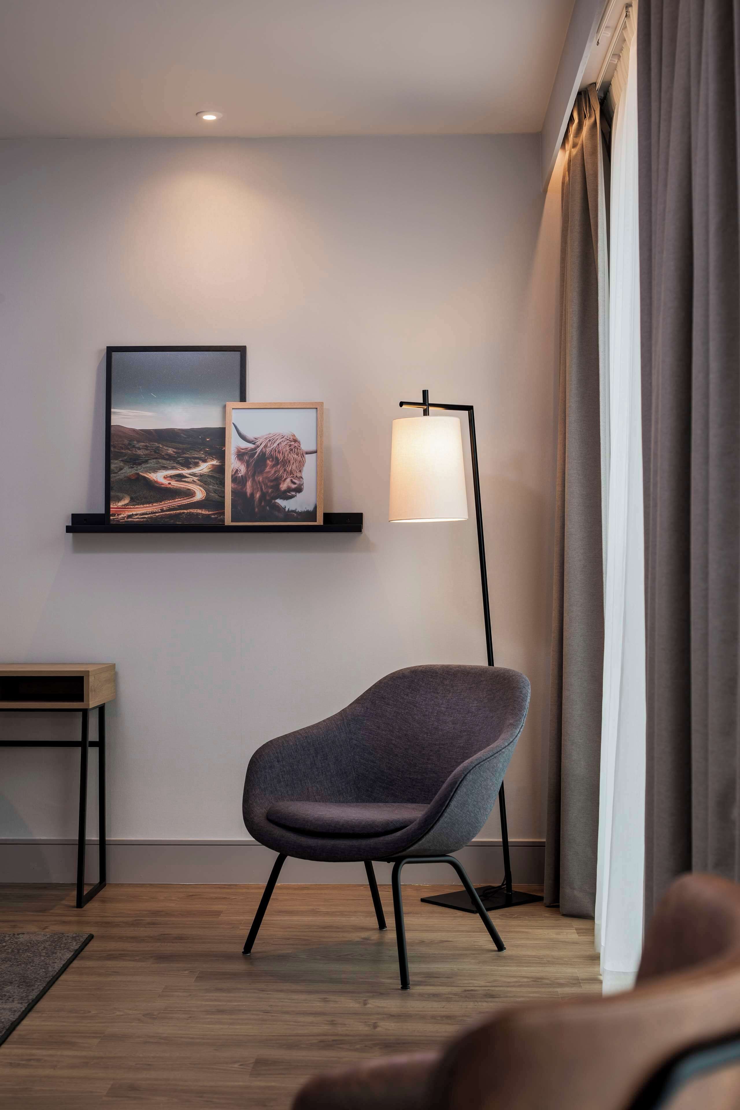 A modern room with a grey armchair, a floor lamp, and two framed pictures on a wall.