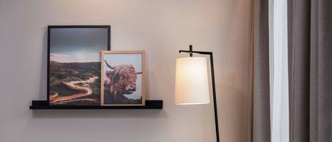 A modern room with a grey armchair, a floor lamp, and two framed pictures on a wall.