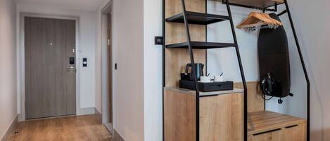 A compact room with a wooden wardrobe, a small desk, and a hanging shelf with a coat rack.