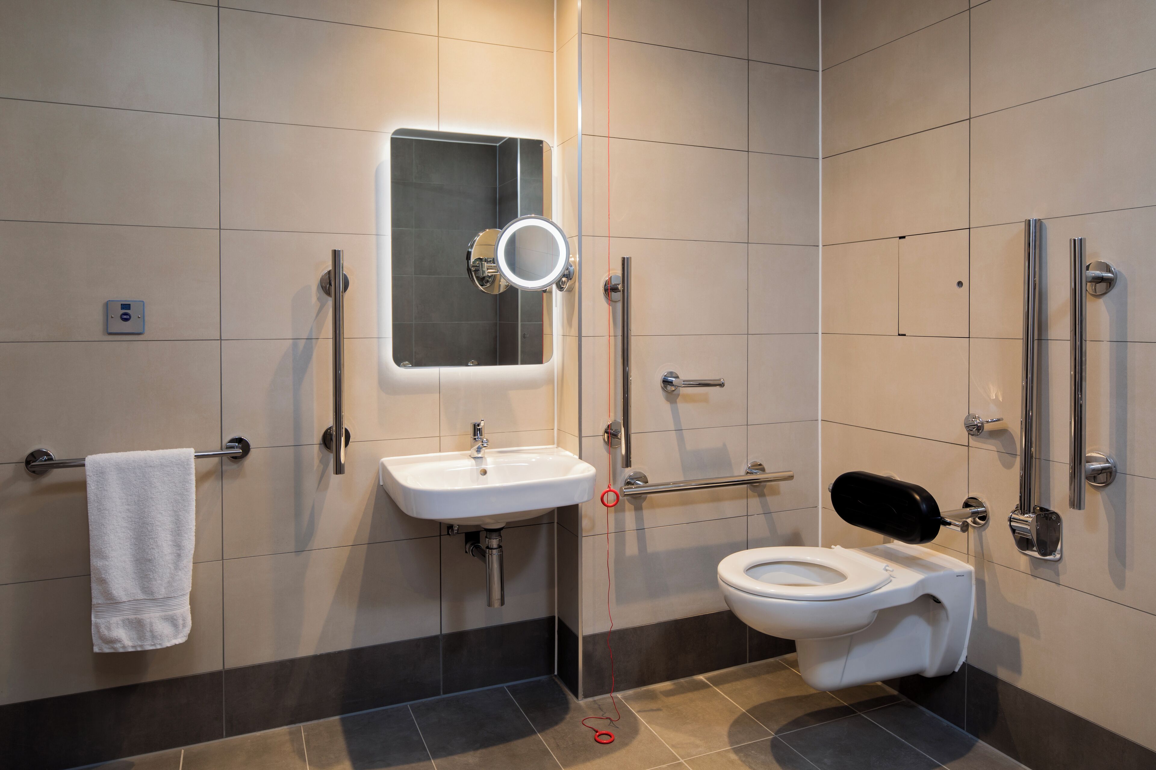 A modern bathroom with a white sink, a mirror, a toilet, and a handrail.