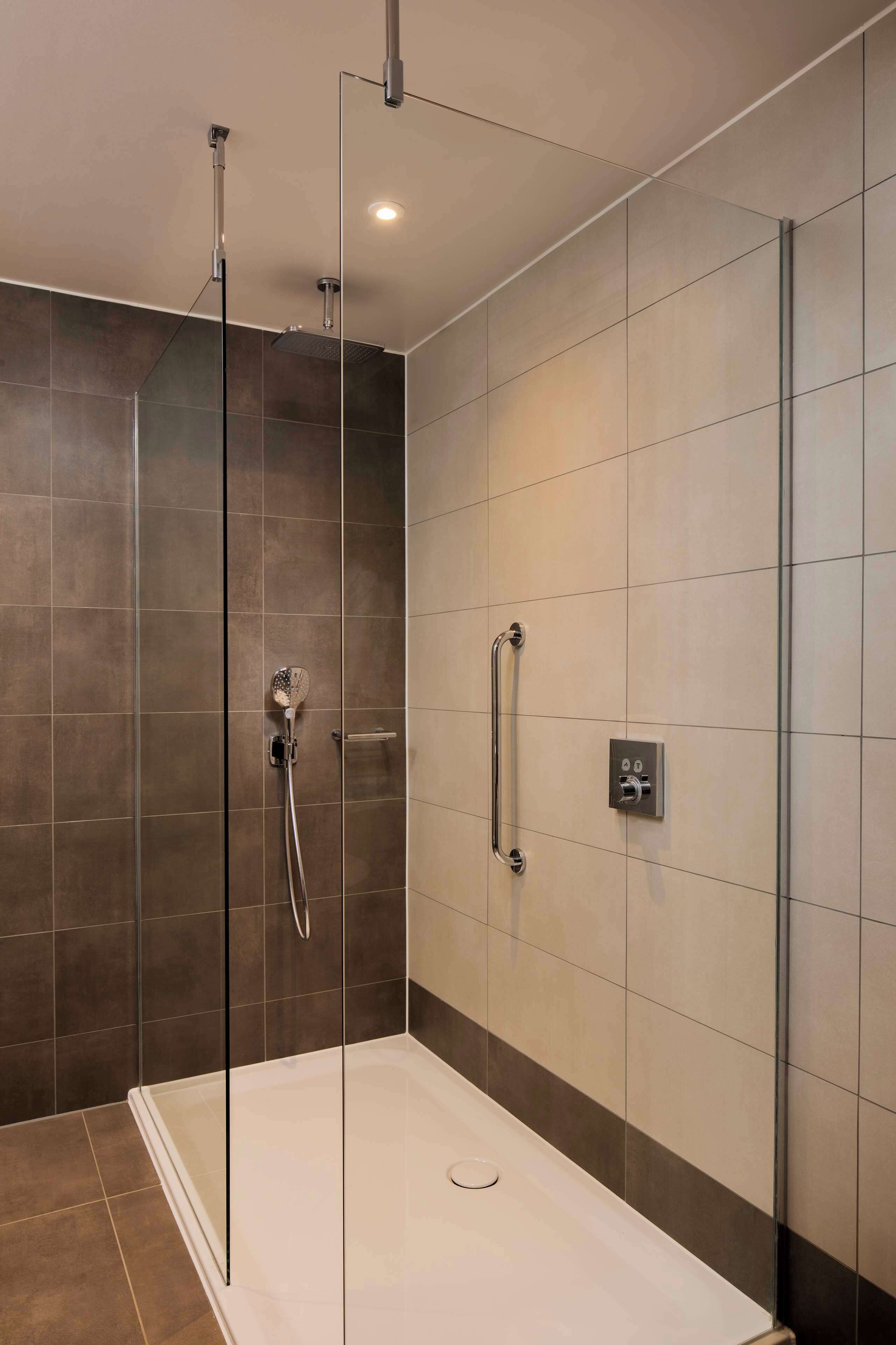 A modern shower with a glass enclosure, a handheld showerhead, and a wall-mounted control panel.