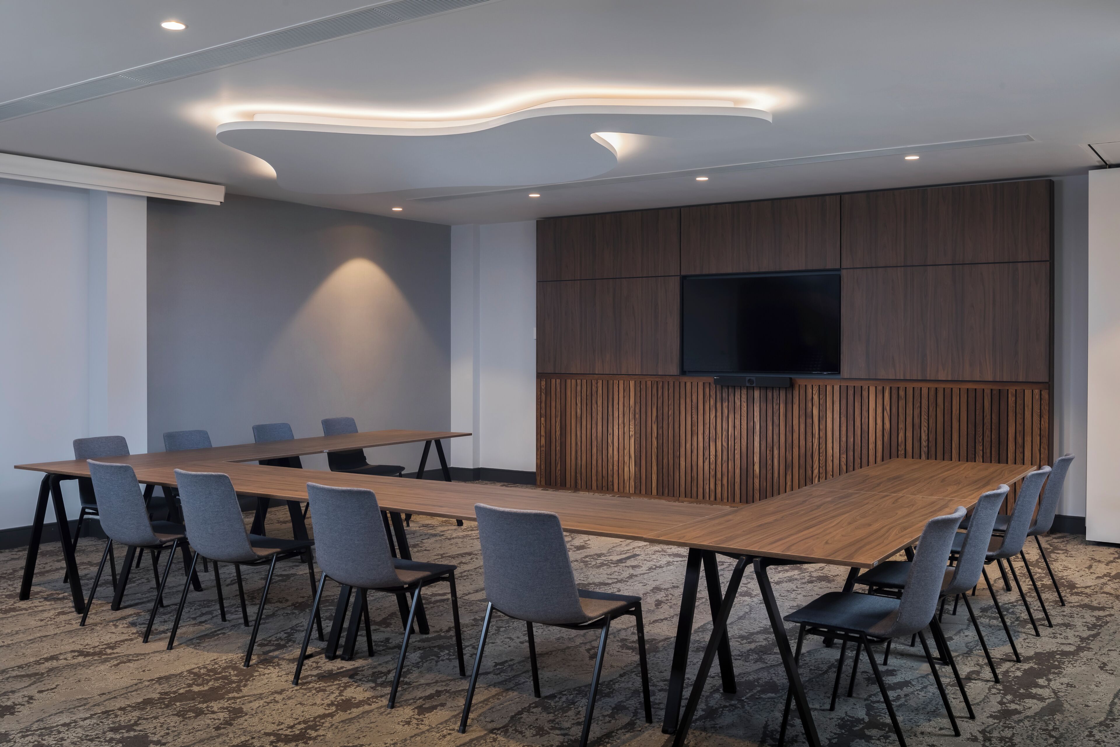 A conference room with a long table and chairs, a flat-screen TV, and wooden paneling on the wall.