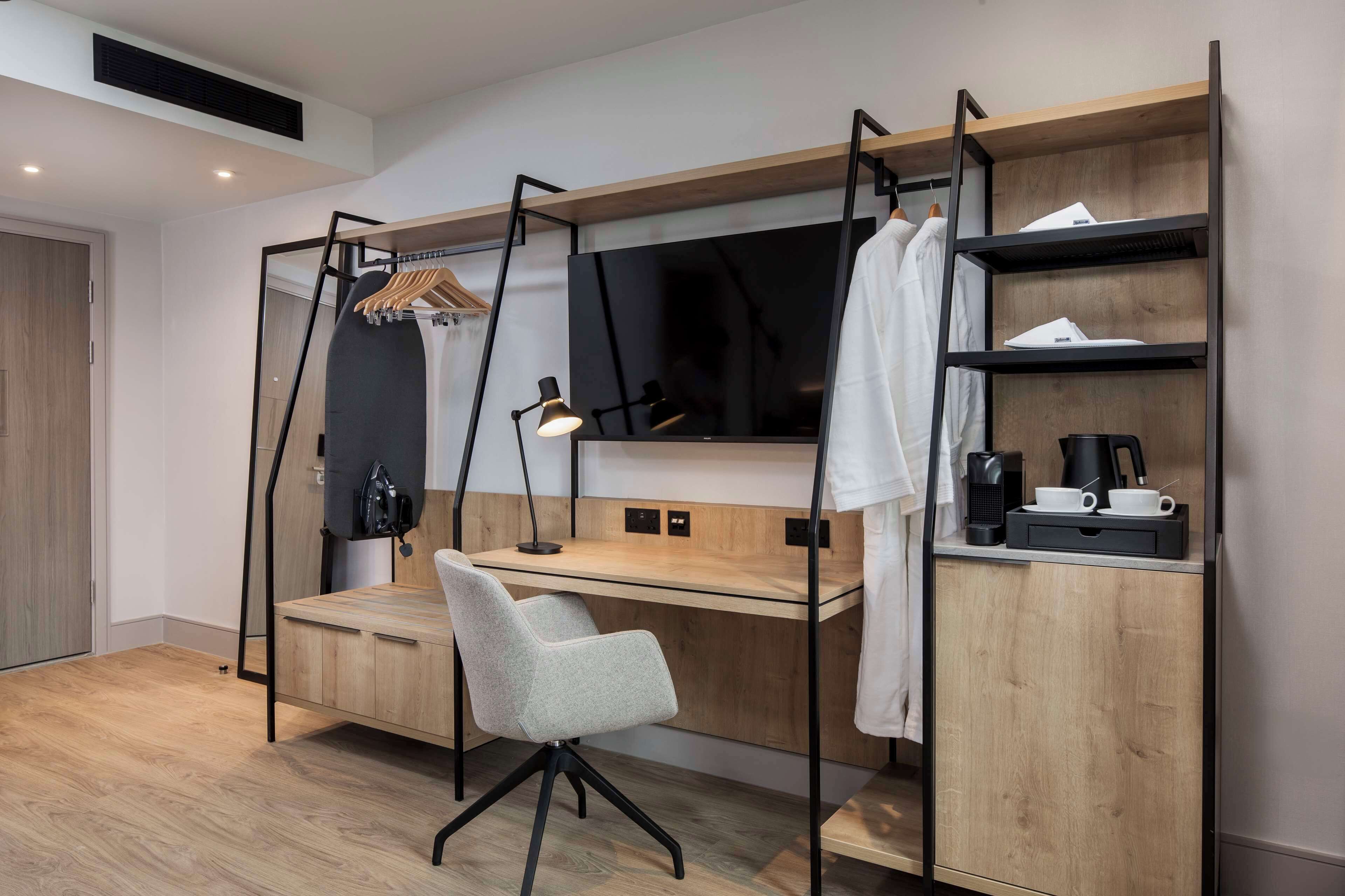 Een moderne slaapkamer met een houten bureau, een stoel, een televisie en een plank met een koffiezetapparaat.