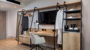 A modern bedroom with a wooden desk, a chair, a TV, and a shelf with a coffee maker.