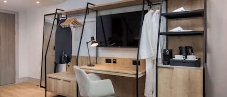 A modern bedroom with a wooden desk, a chair, a TV, and a shelf with a coffee maker.