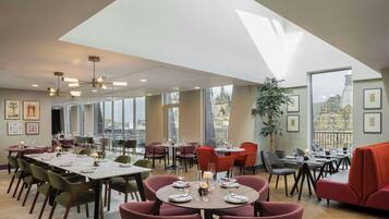 A spacious dining area with multiple tables and chairs, large windows offering city views, and a modern ceiling design.