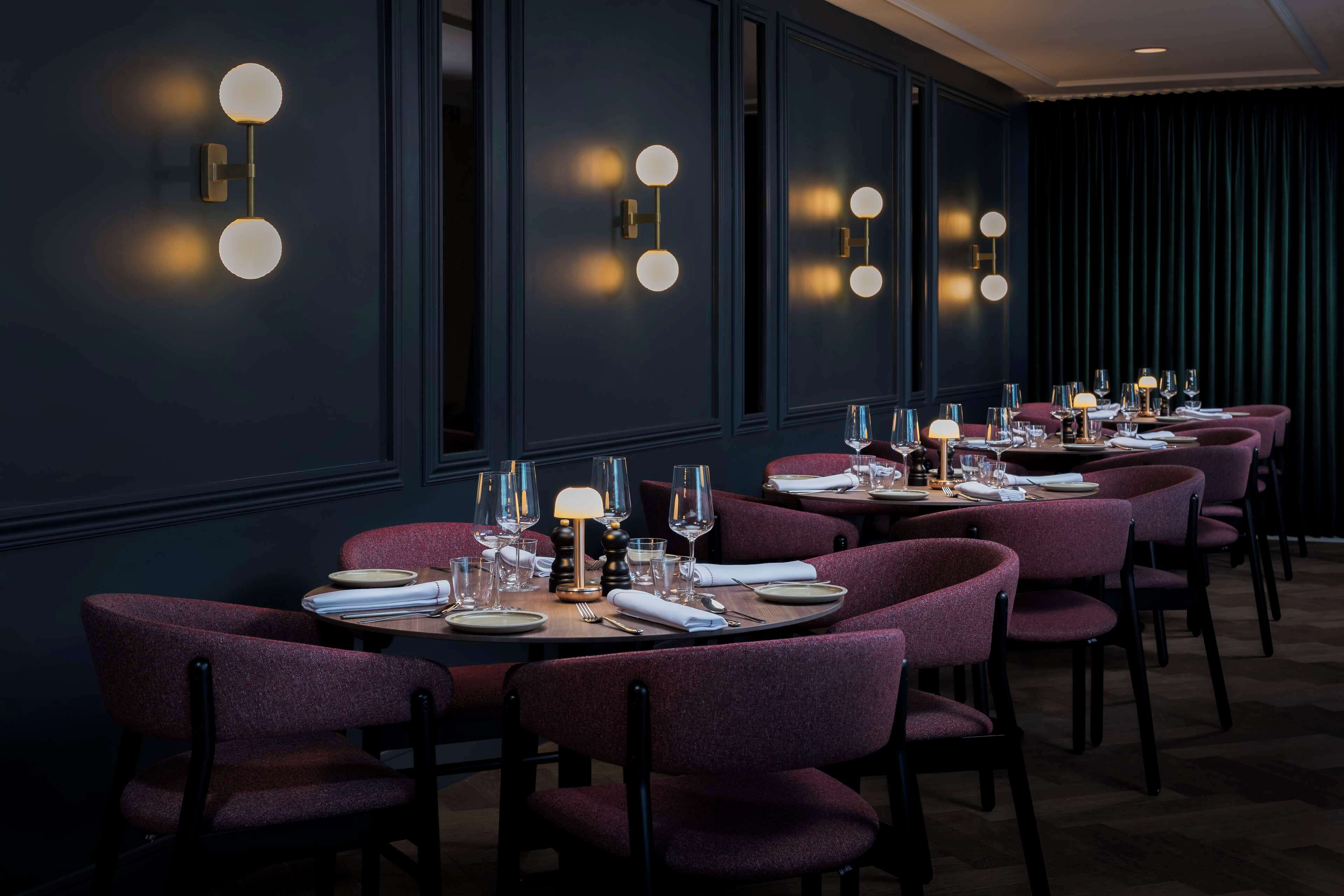 Un restaurante con paredes oscuras, mesas redondas y sillas moradas.