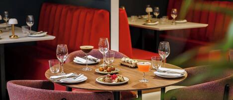 A restaurant interior with red upholstered booths and round tables, each set with plates, cutlery, and glasses.