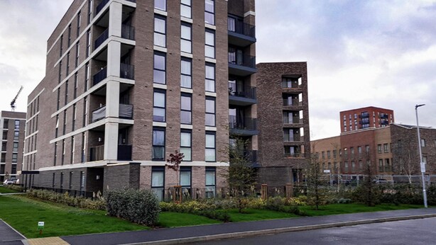 A multi-story residential building with a brick facade, balconies, and a landscaped front yard.