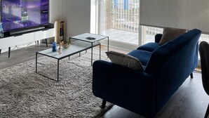 A modern living room with a flat-screen TV, a blue sofa, and a glass coffee table.