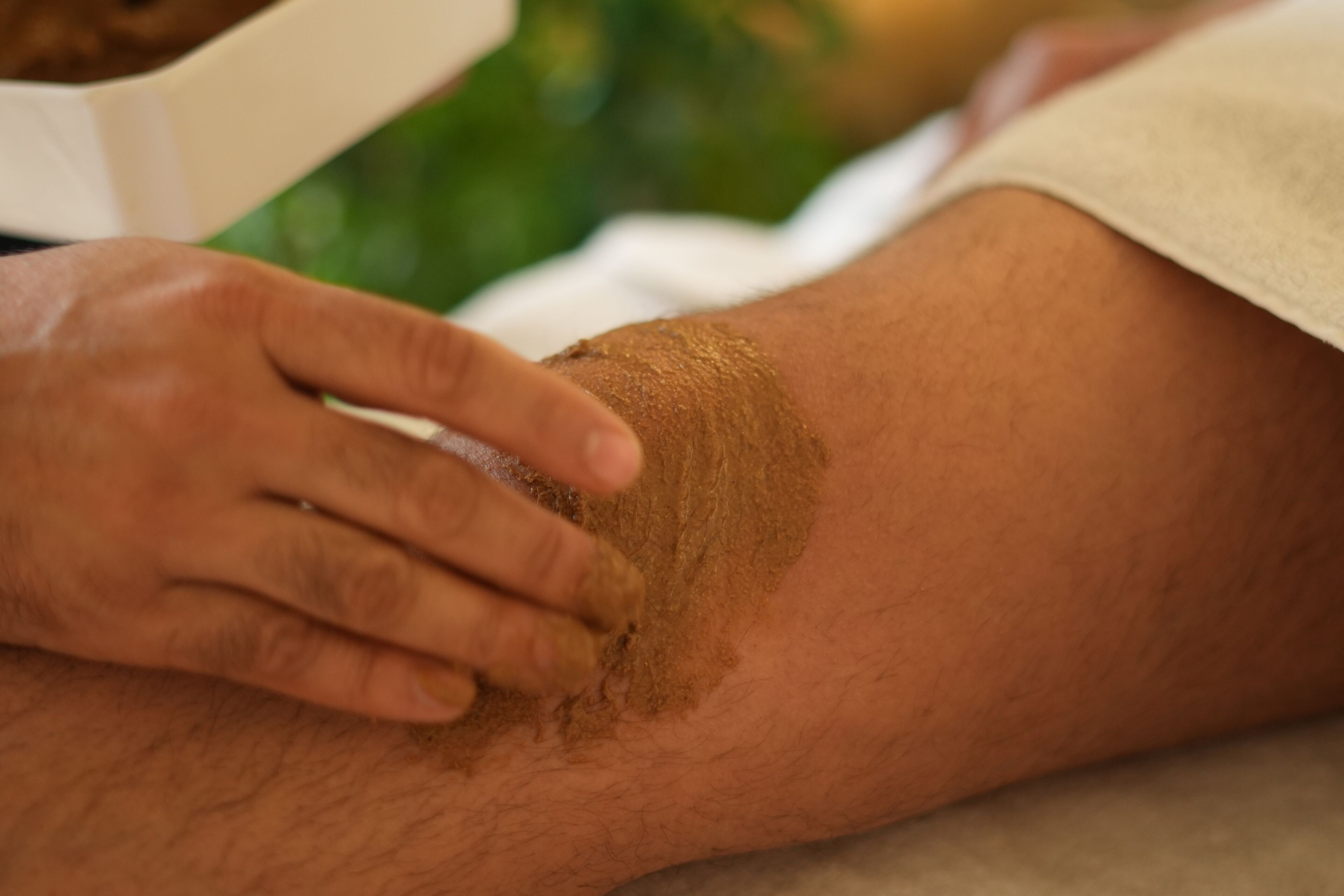 A close-up of a person's arm with a hand applying a brown substance to the skin.