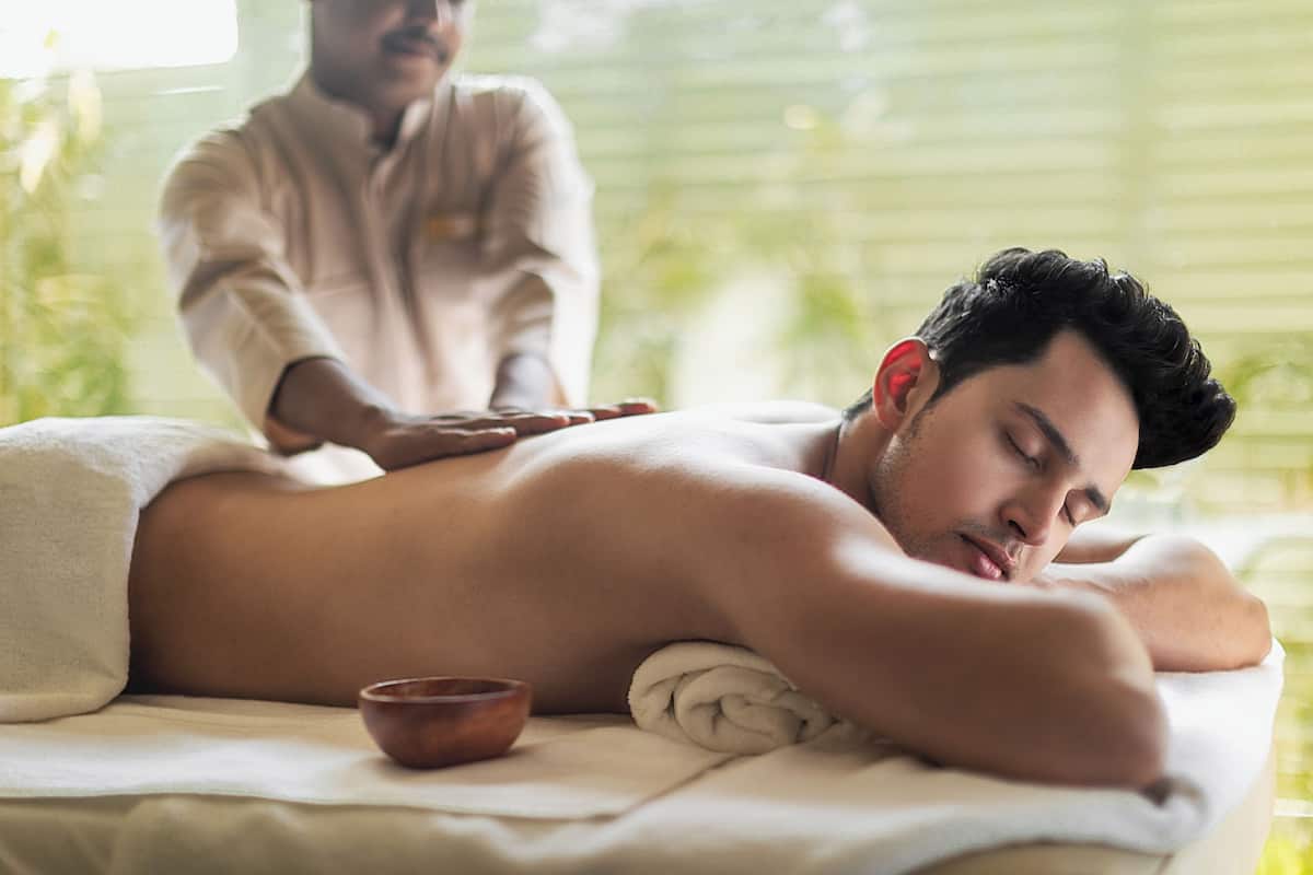 A person receiving a massage in a room with a window and a small wooden bowl on the massage table.