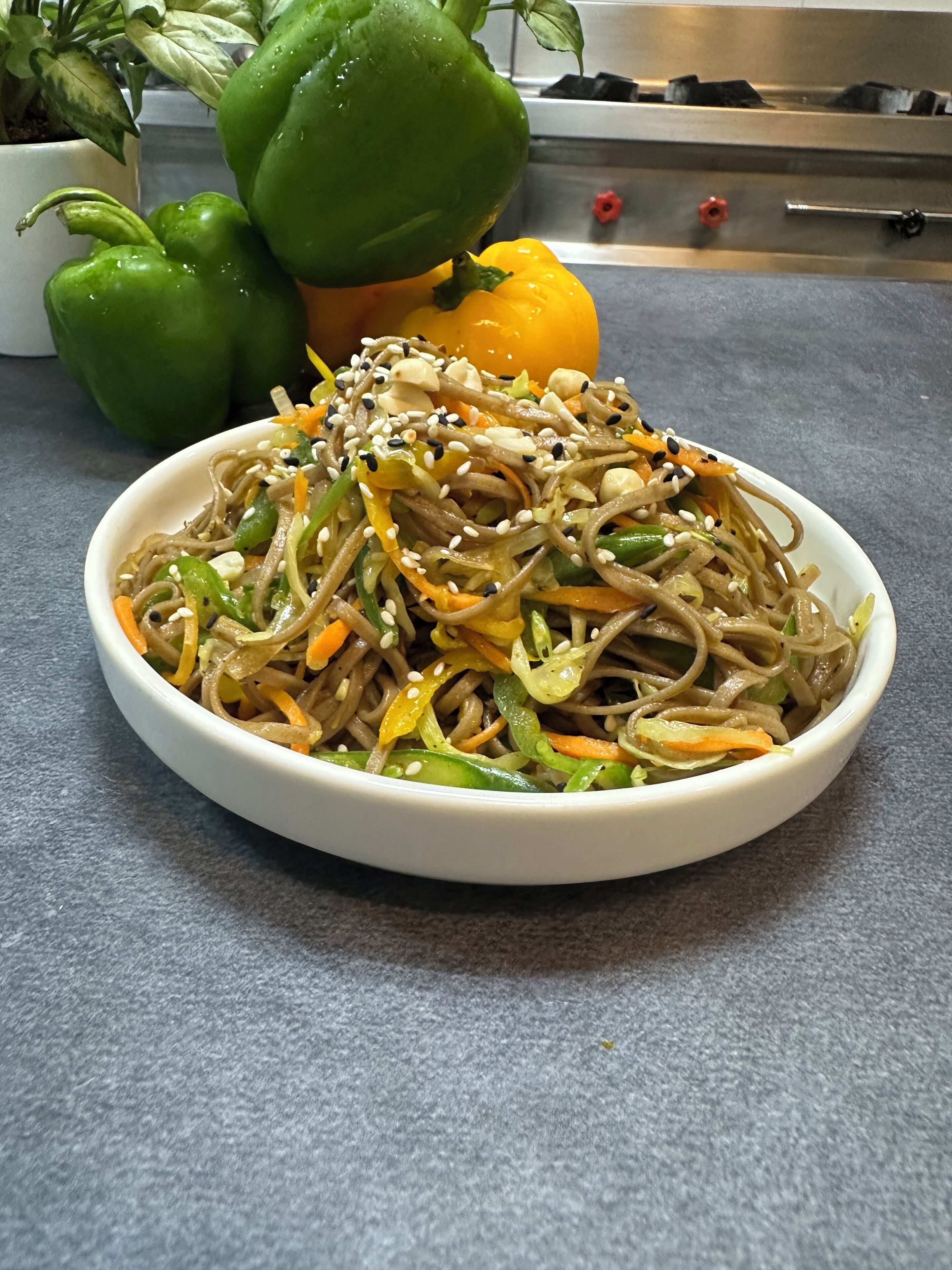 Un tazón de fideos con verduras y semillas de sésamo sobre una encimera gris.