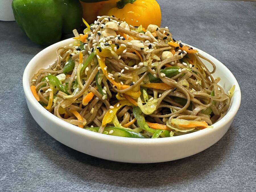 Un tazón de fideos con verduras y semillas de sésamo sobre una encimera gris.